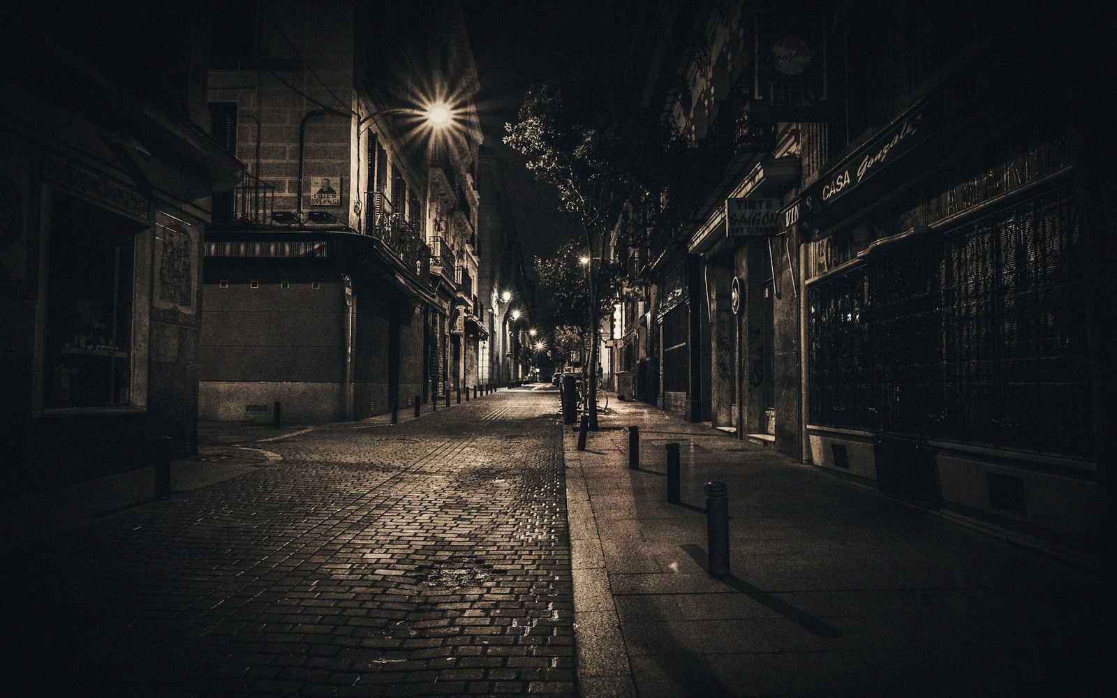 Empty cobblestone street glowing under a single streetlamp at night with shuttered shopfronts
