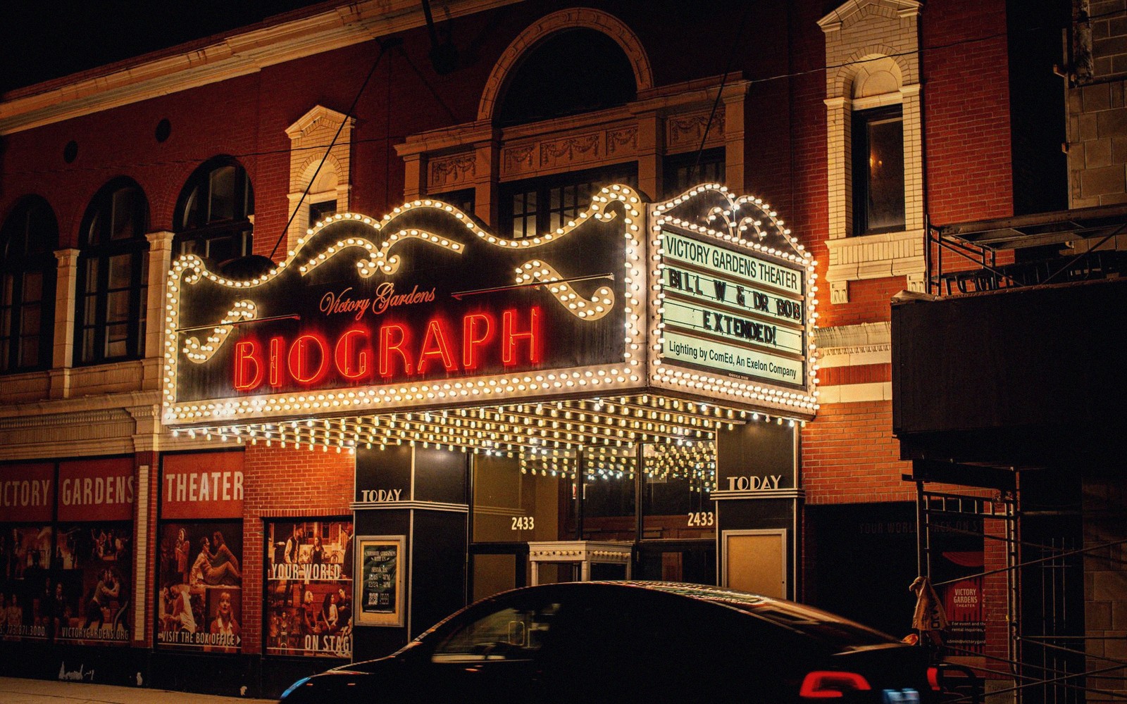 The Biograph theater's illuminated marquee glows above a brick facade at night