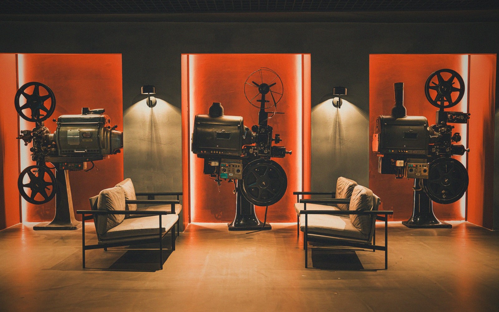 Three vintage film projectors displayed against glowing orange alcoves with modern lounge chairs